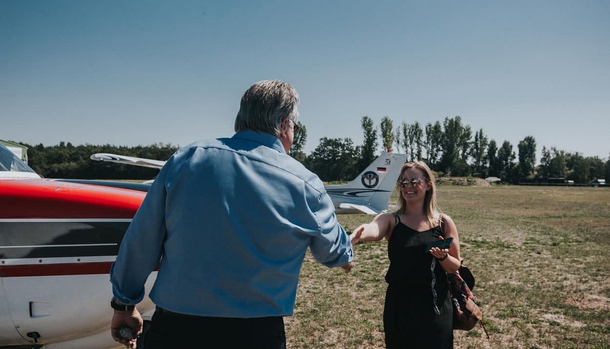 Mann und Frau schütteln sich vor einem Flugzeug die Hand.